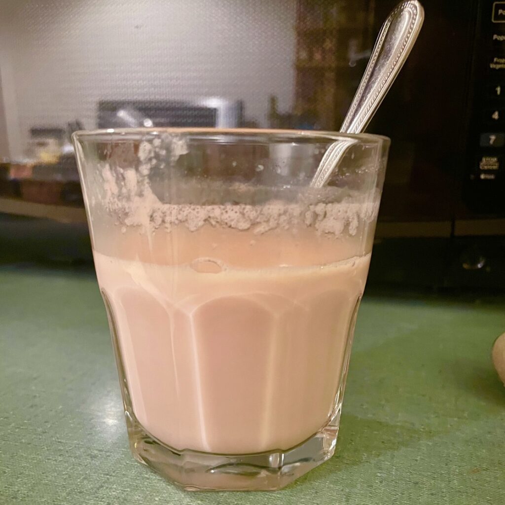 Hot Strawberry White Chocolate n a glass cup with a metal spoon.