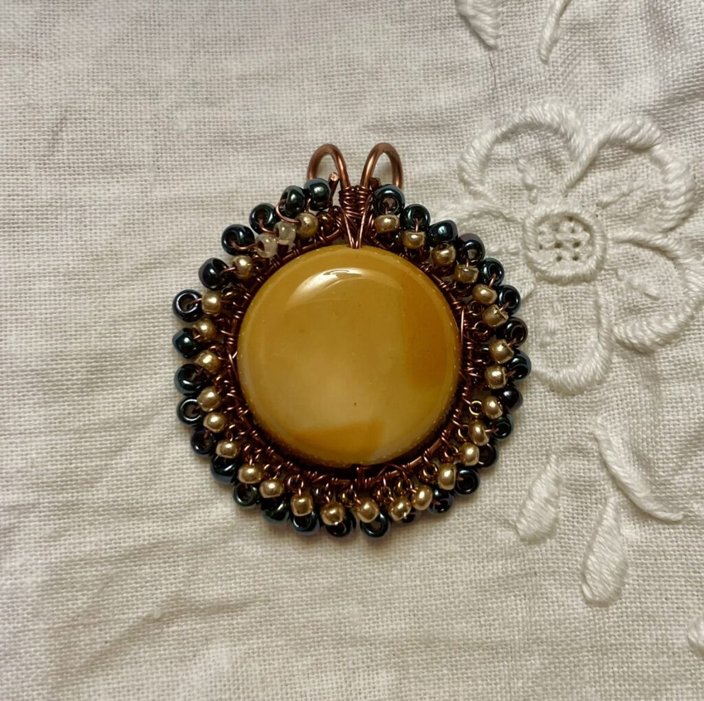 Circular Yellow Mookaite stone surrounded by dark blue and gold beads. Woven together on copper wire.
