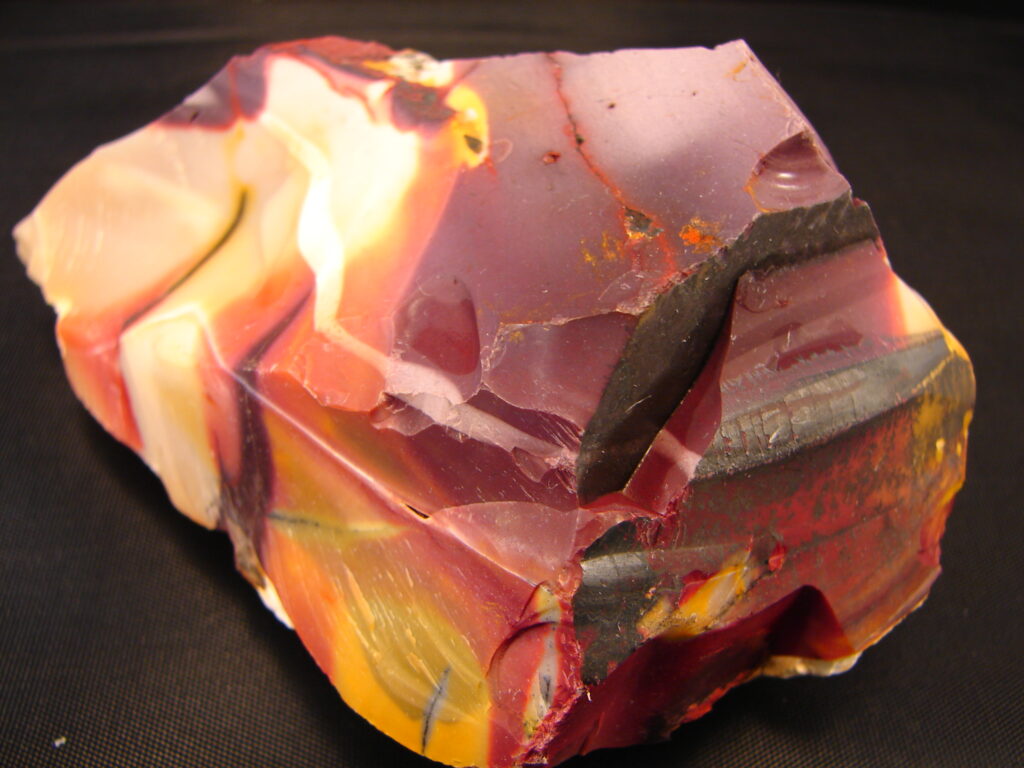 A rough chunk of red, orange, yellow, and cream stripped mookaite