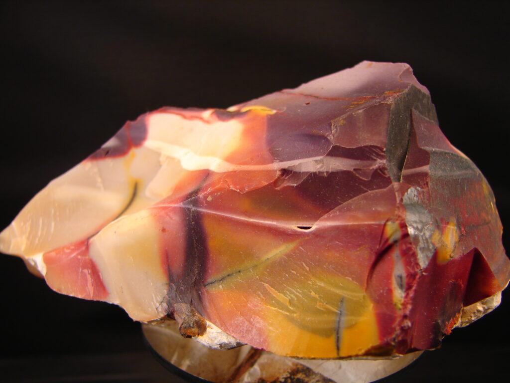 A rough chunk of red, orange, yellow, and cream stripped mookaite